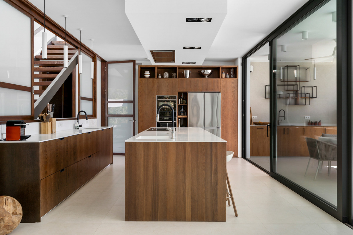 Spacious kitchen featuring a large central island, wood cabinetry, built-in appliances, and sliding glass doors.