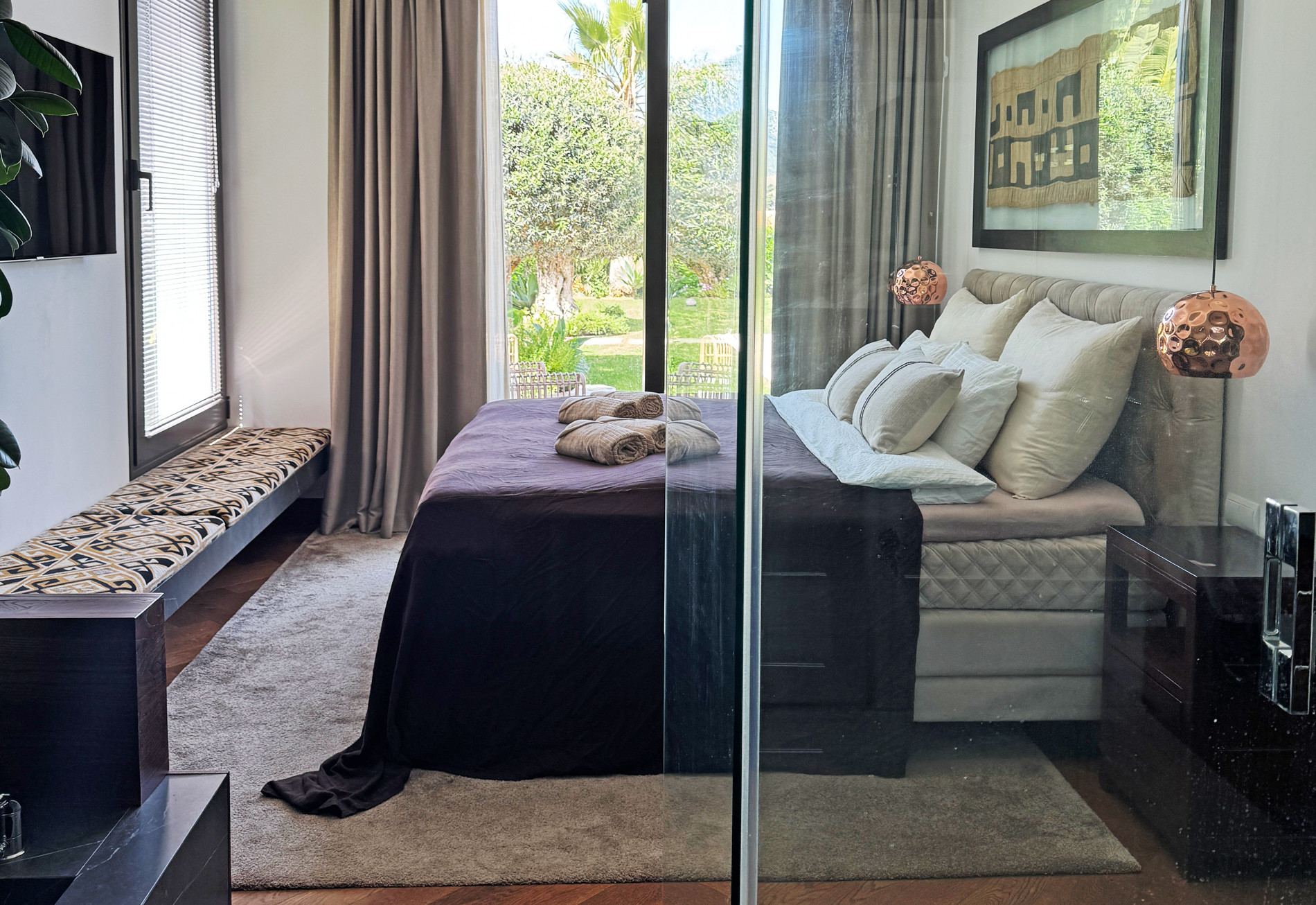 Bedroom with a large bed, glass partition, and a view of an outdoor garden area.