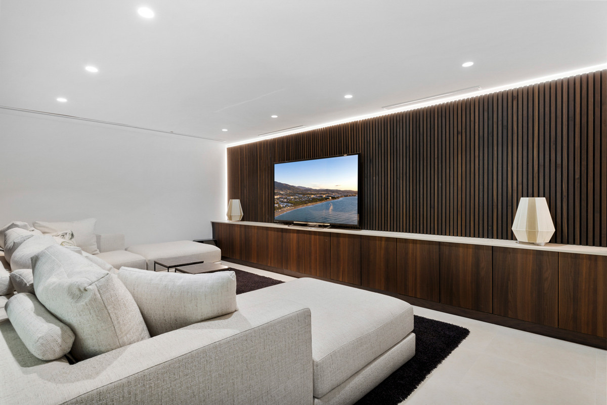 Modern living room with light sectional sofas, a large wall-mounted TV, and dark wood slat wall accents.