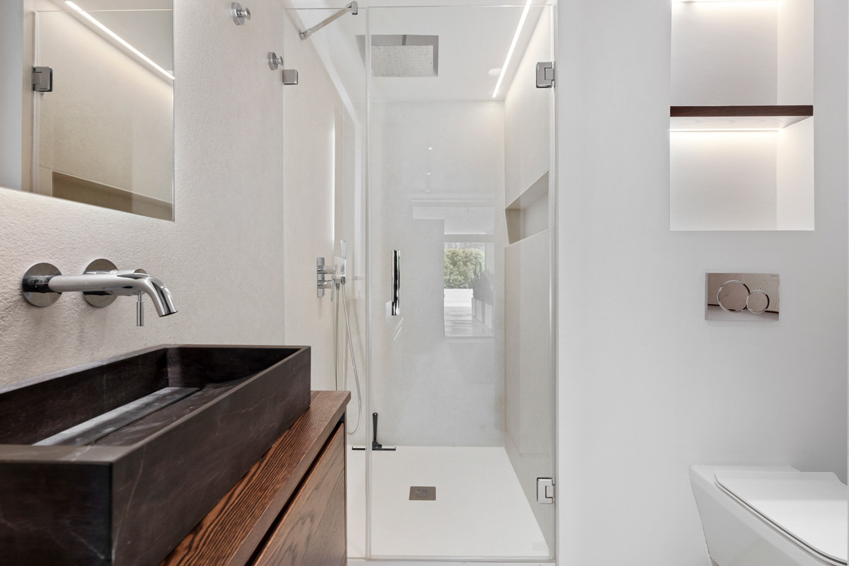 Modern bathroom with a glass-enclosed shower, dark vessel sink on a wood vanity, and white wall-mounted toilet.