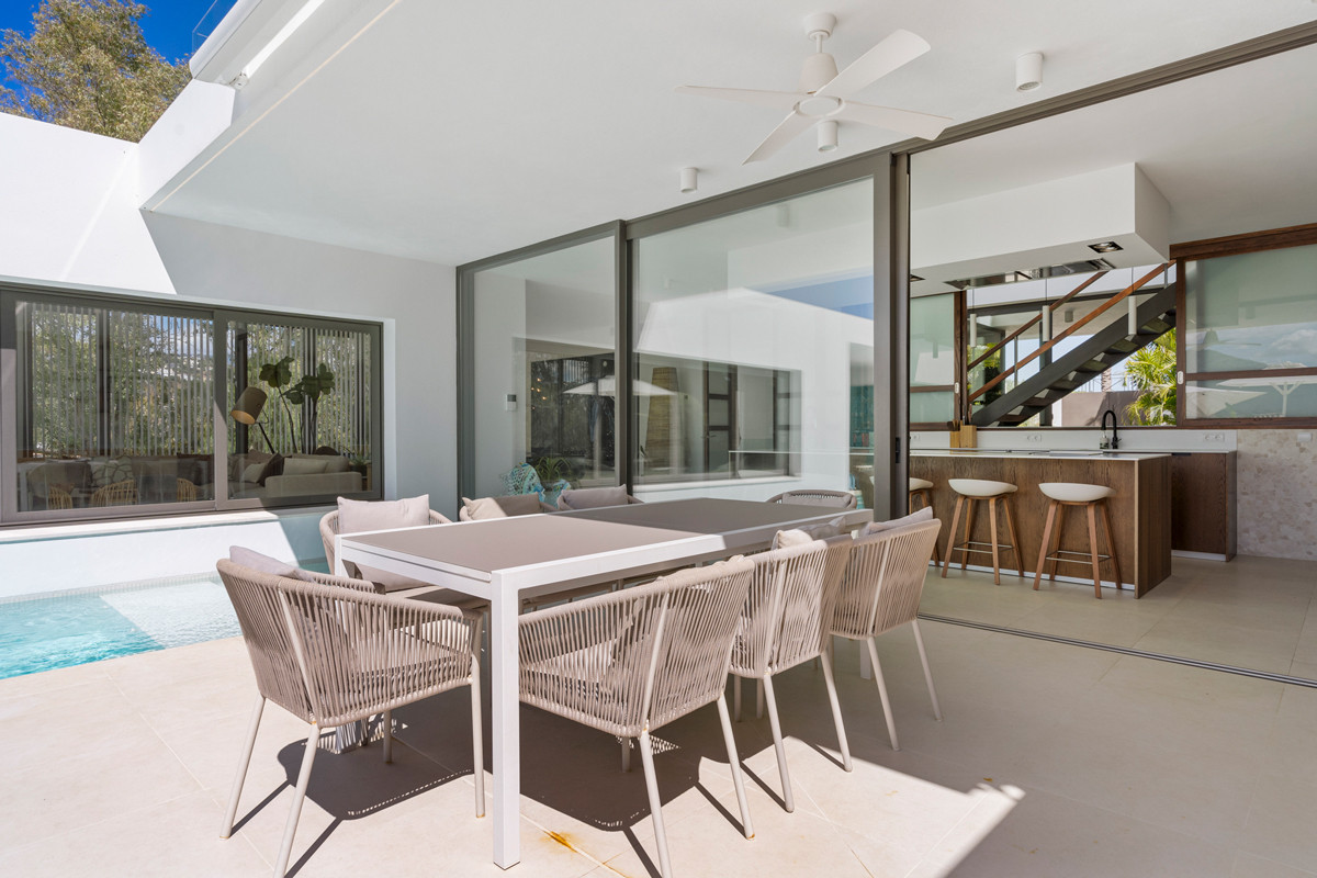 Covered outdoor dining area with a modern table and chairs, overlooking a pool and interior bar.