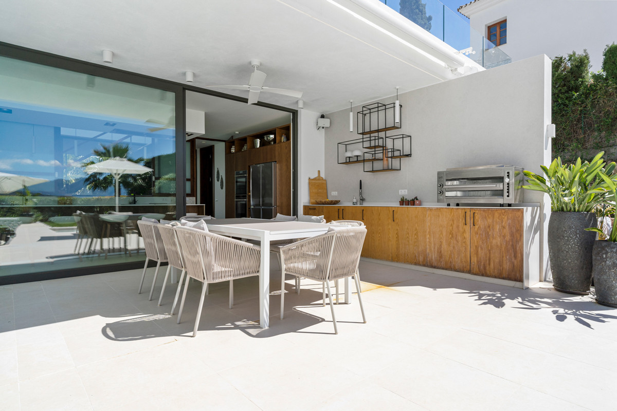 Outdoor kitchen and dining area on a patio, with an oven, grill, and sliding glass doors to interior.