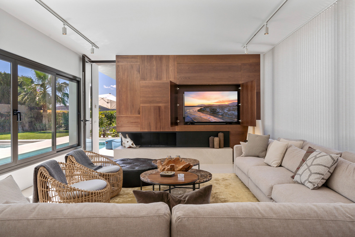 Living room with large sofa, patterned pillows, wooden feature wall with television, and access to a pool patio.