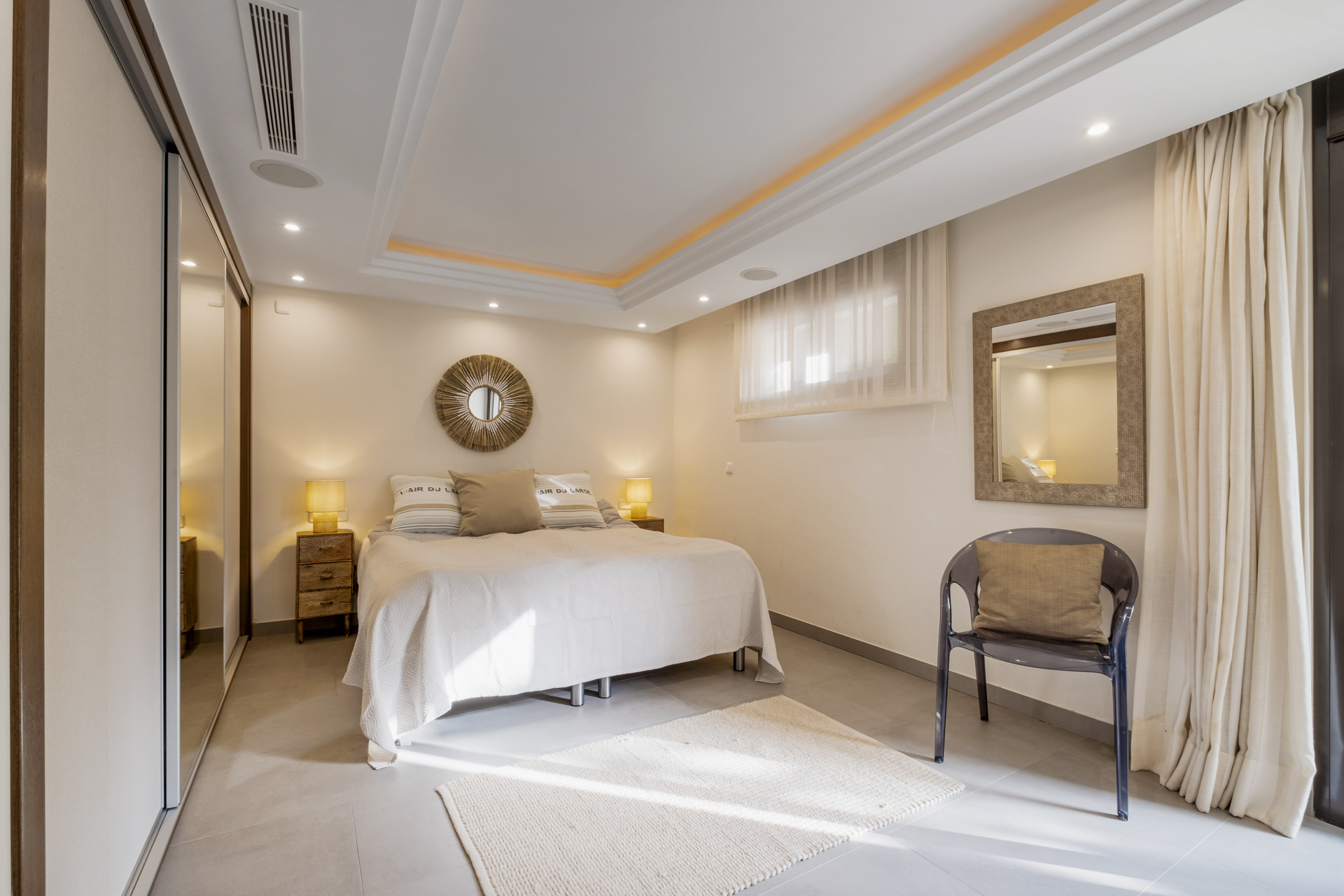 Bright bedroom with a large bed, mirror, and soft lighting.