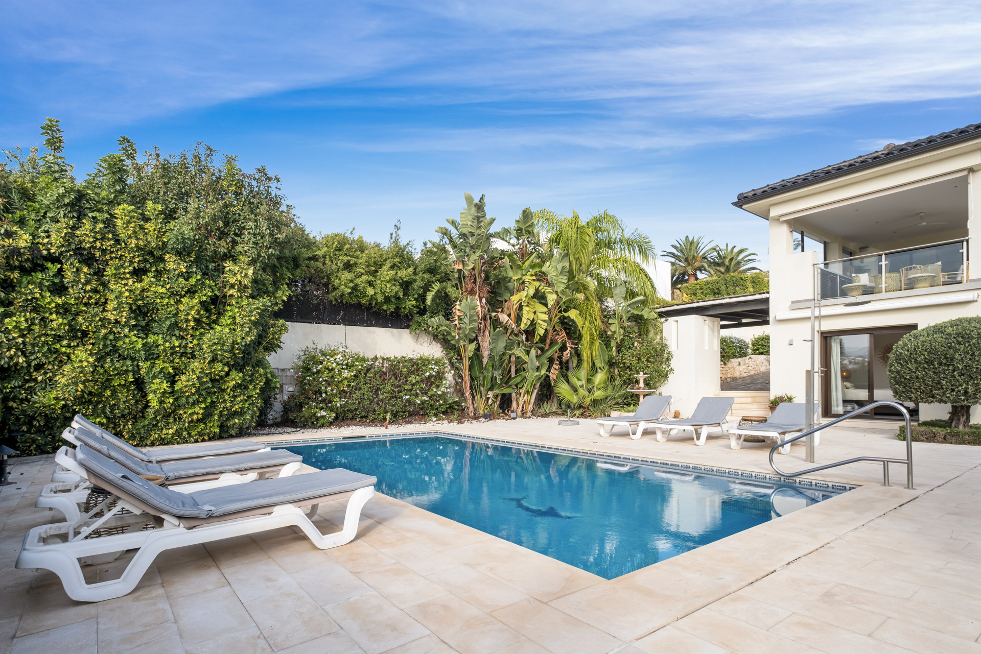 Swimming pool surrounded by sun loungers and lush greenery.