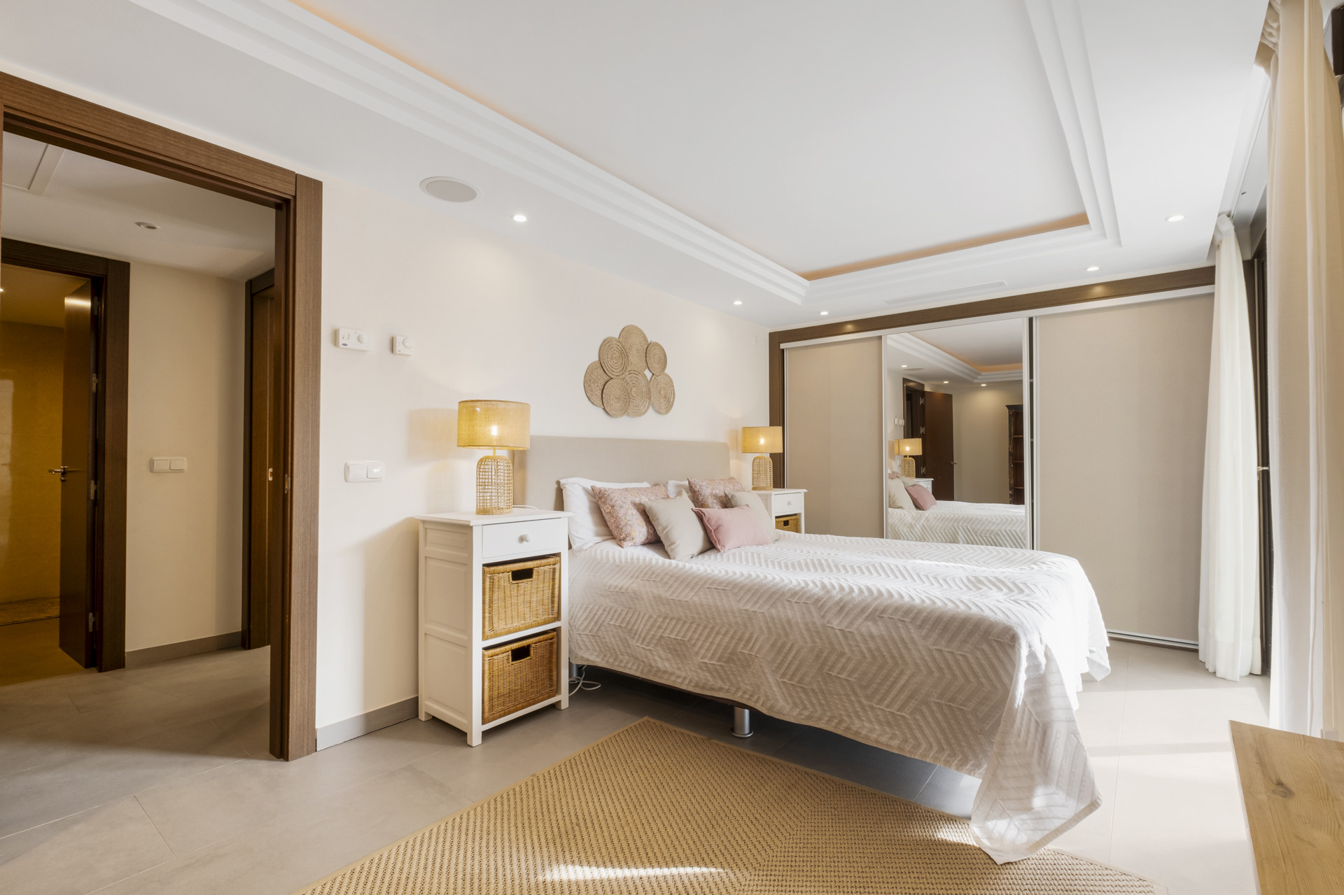 Bedroom with a double bed, decorative pillows, and a lamp beside a white nightstand.