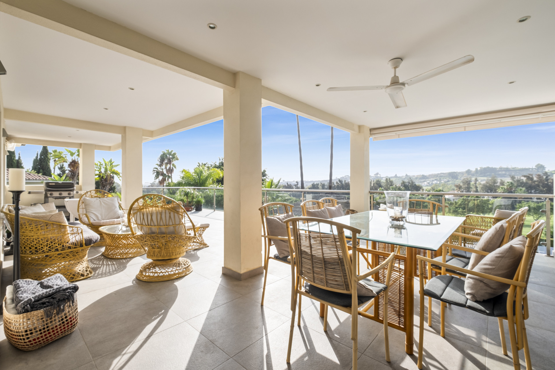 Spacious terrace with wicker furniture and dining table overlooking greenery.