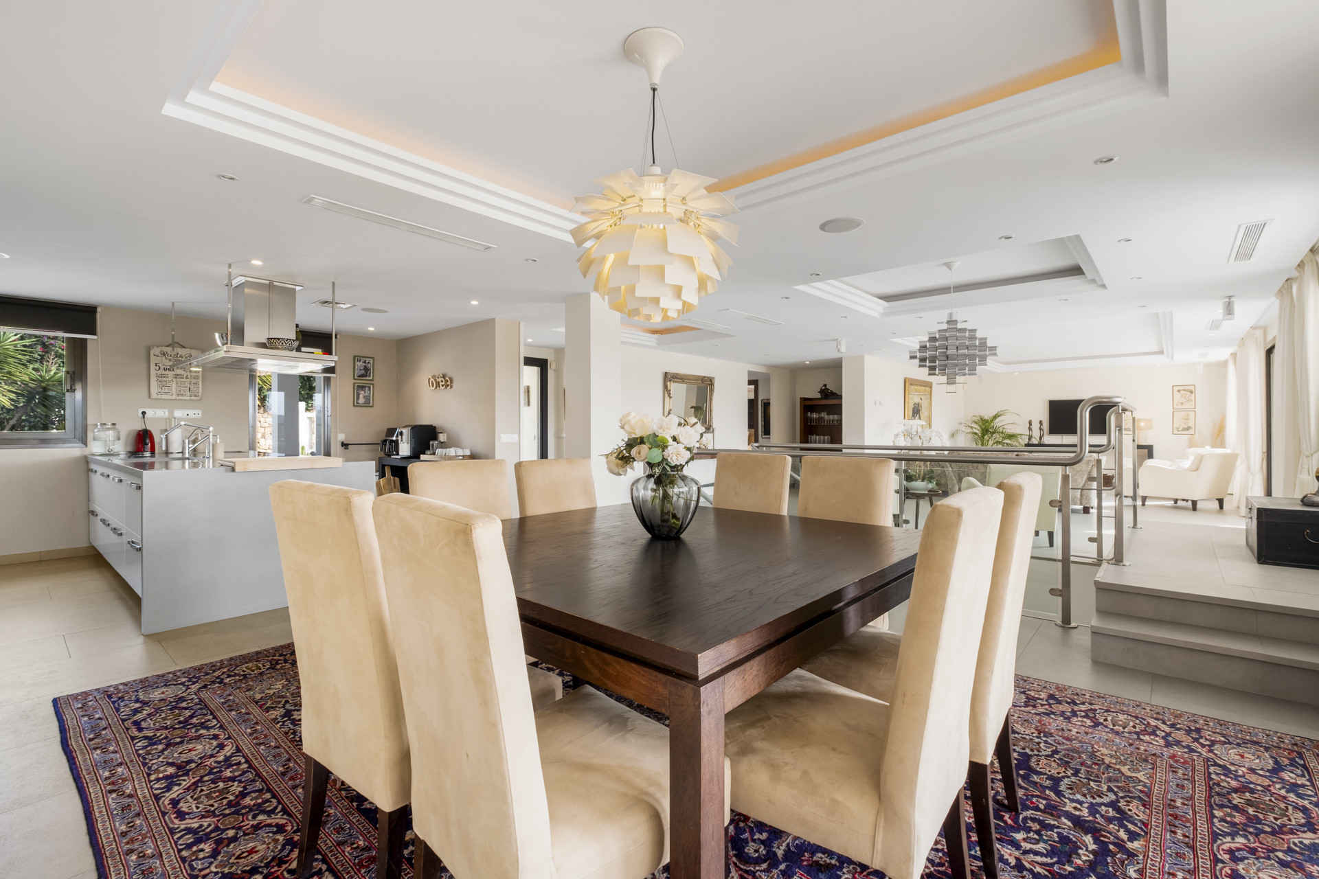 Dining area with a wooden table, beige chairs, and contemporary light fixture above.