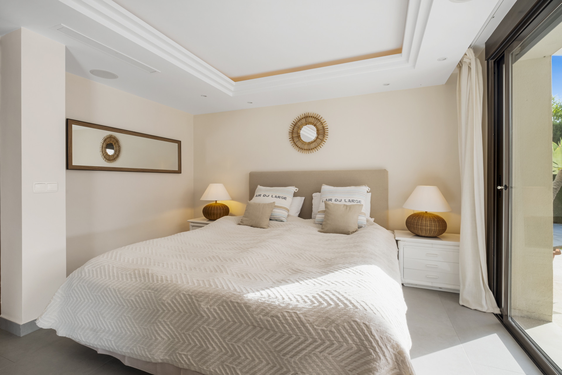 Cozy bedroom with a mirror, bedside lamps, and cream-colored decor.