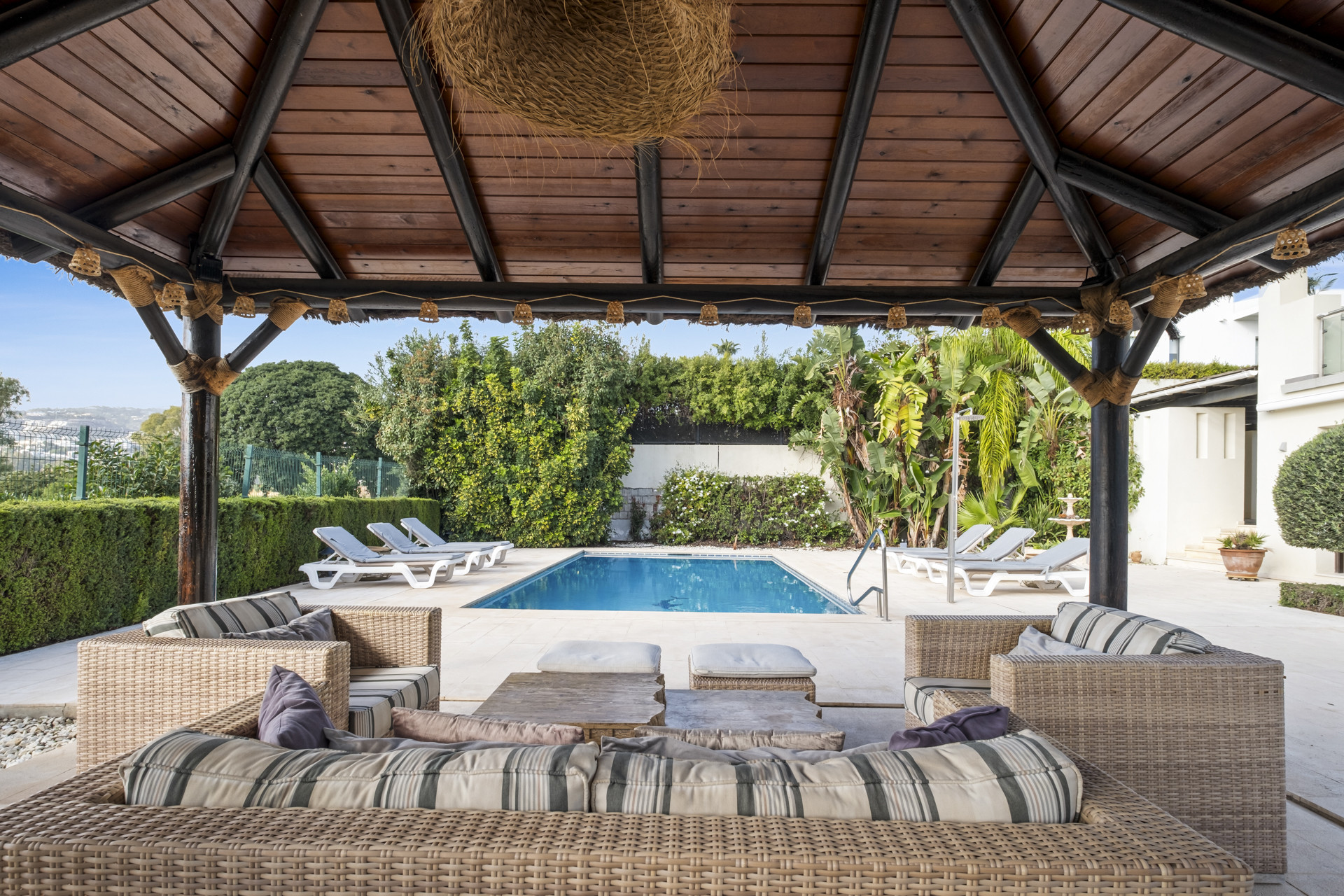Covered seating area with wicker furniture next to swimming pool.