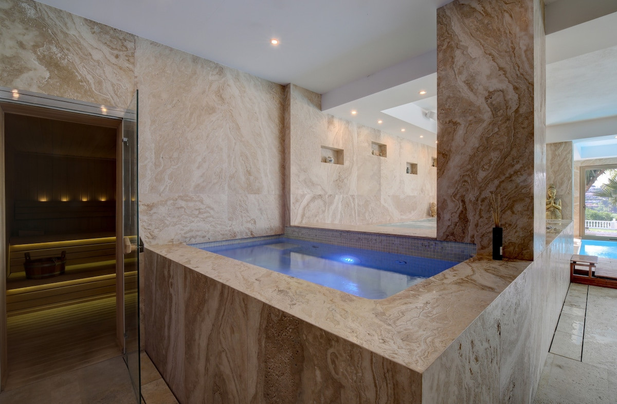 An indoor area with stone walls, a small pool, and a sauna visible behind glass doors.
