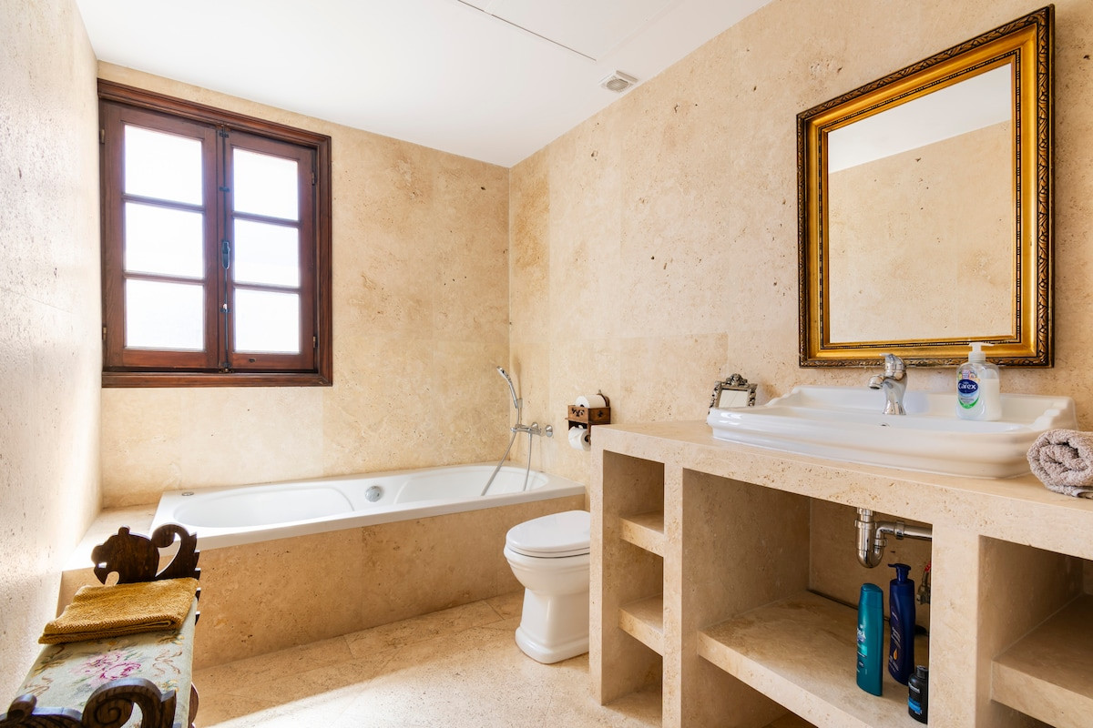 Spacious bathroom features a bathtub, sink, and window with wooden frame.