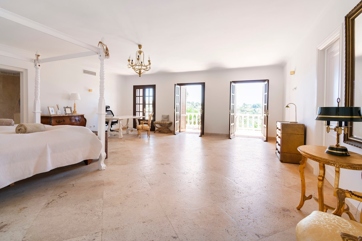 Large bedroom with a four-poster bed, desk, and two double doors leading outside.