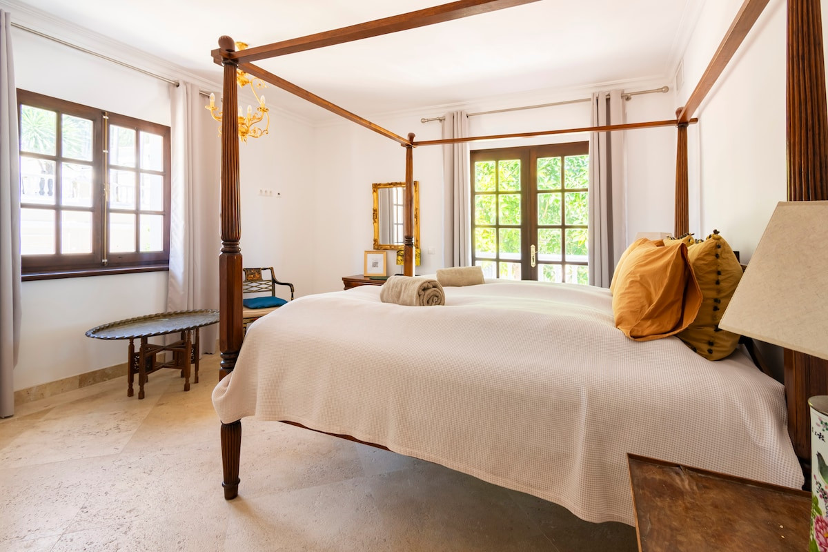 A bedroom featuring a four-poster bed, a mirrored dresser, and natural light from windows.