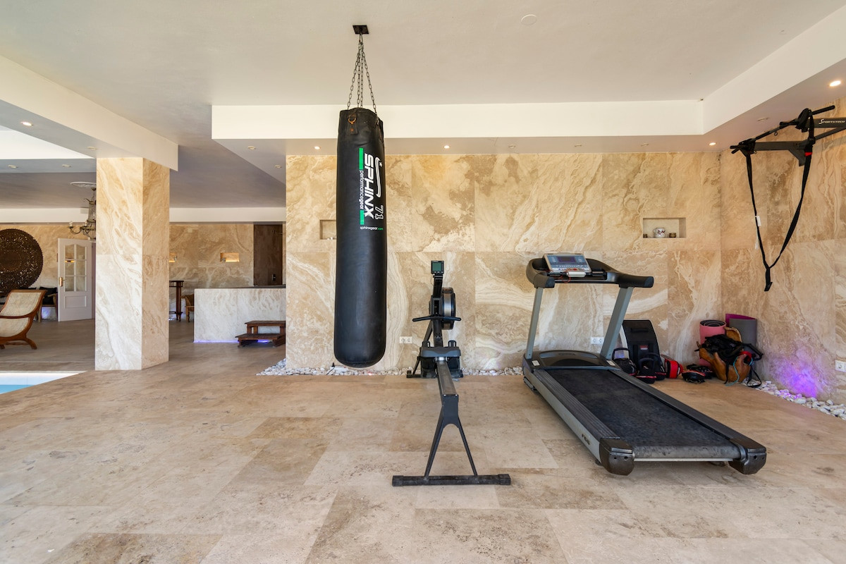 Spacious gym with a boxing bag, treadmill, and rowing machine on tiled flooring.
