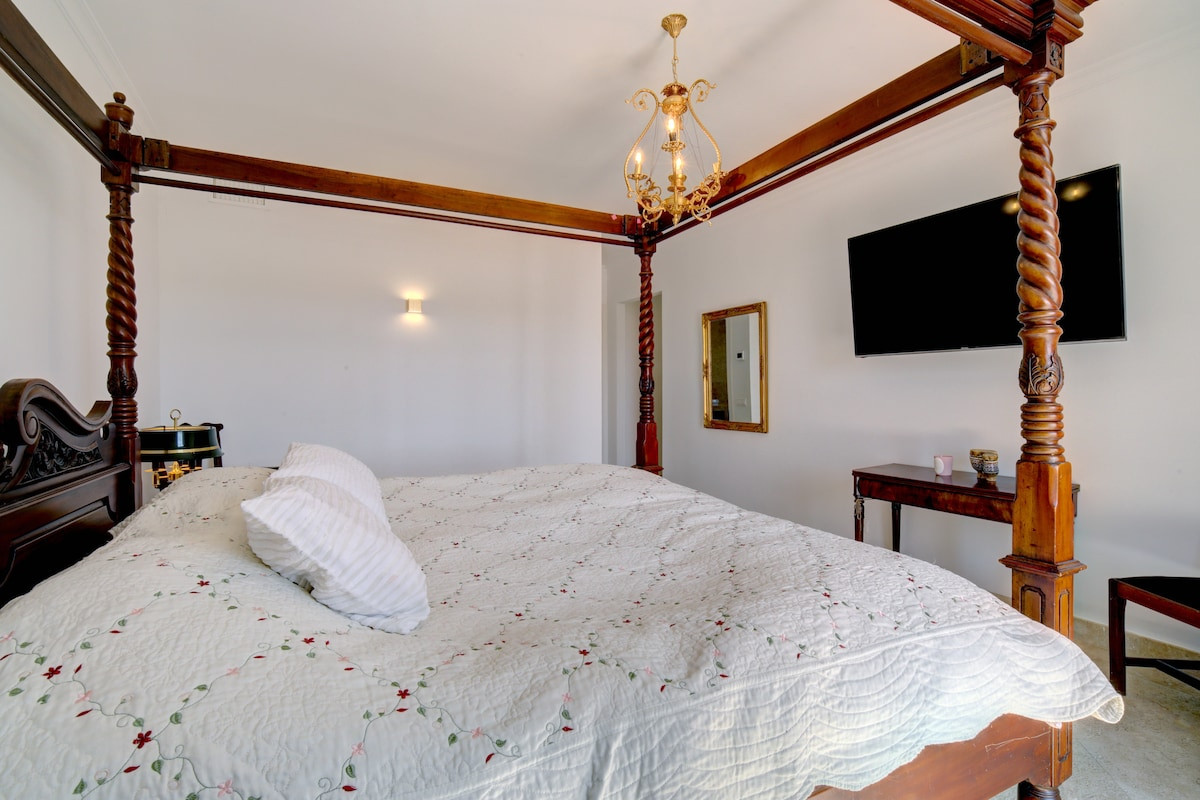 Four-poster bed with chandelier and a large TV on the wall.