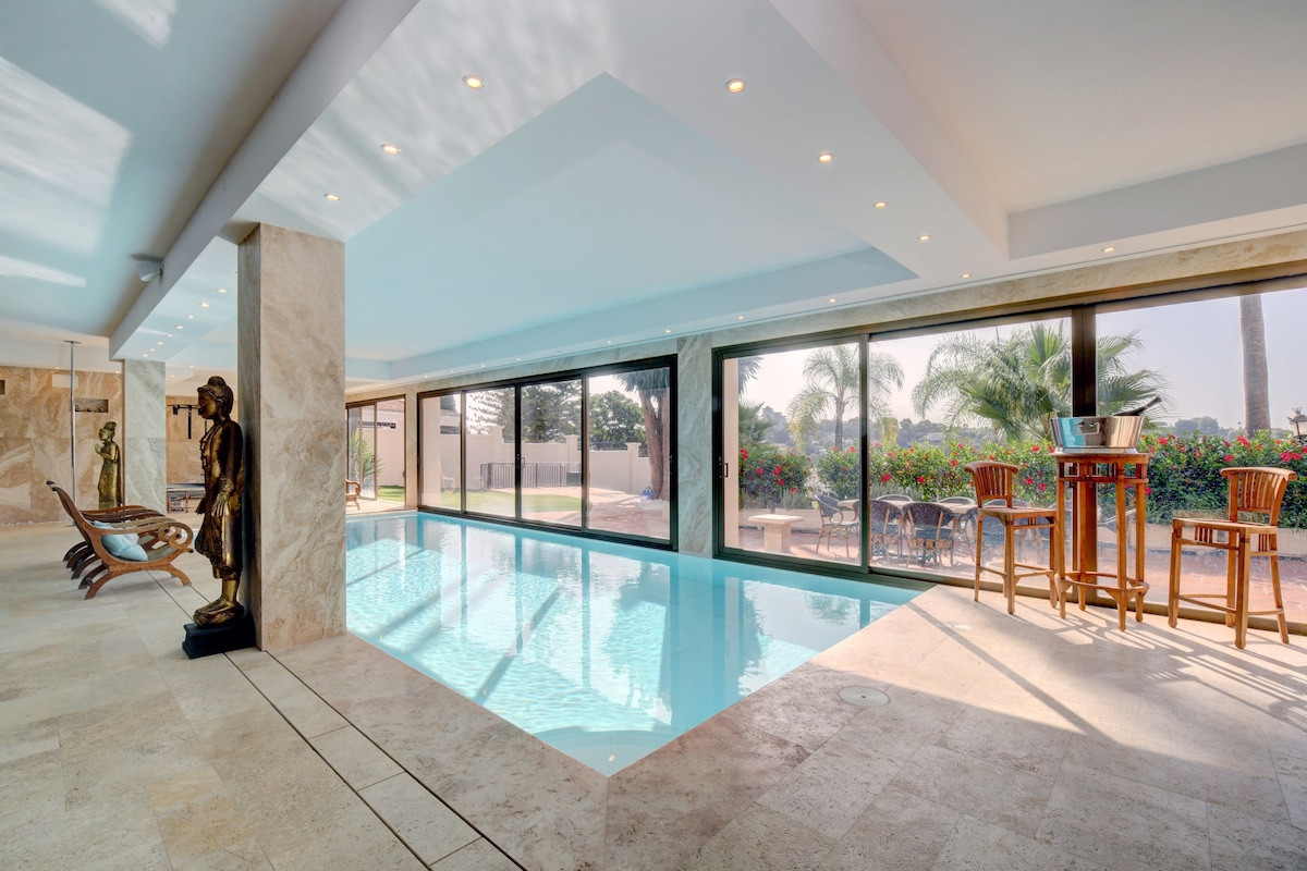Indoor swimming pool area with large windows, a bar space, and sculptures adding decor.