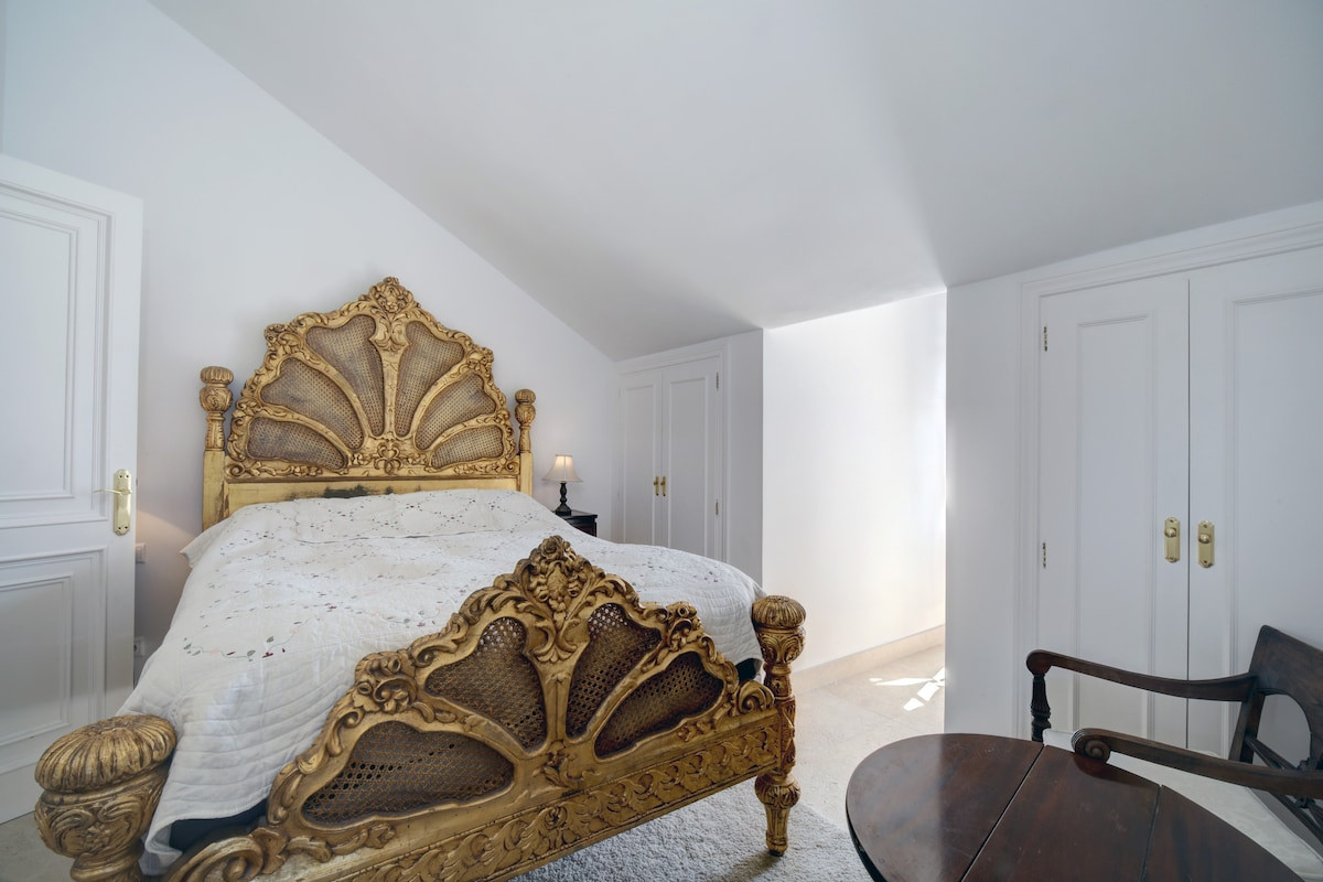 Bedroom with a golden bed frame and white bedding, featuring large built-in closets.