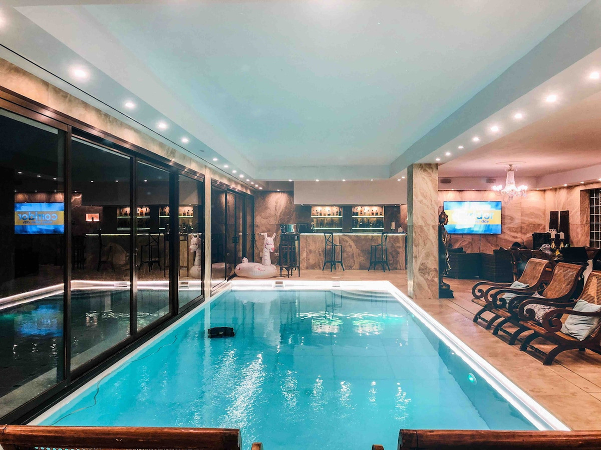 A spacious indoor pool area with a bar, lounge chairs, and large glass doors.