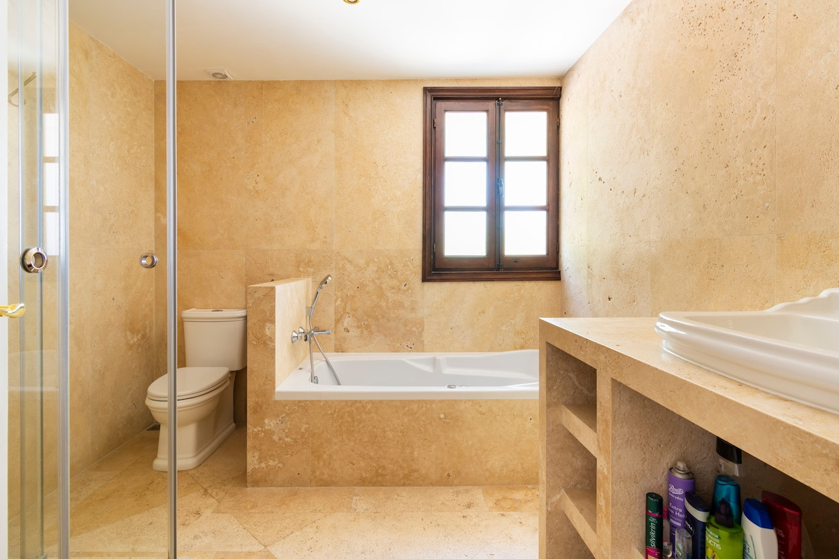 Modern bathroom with bathtub, toilet, and wooden window providing natural light.