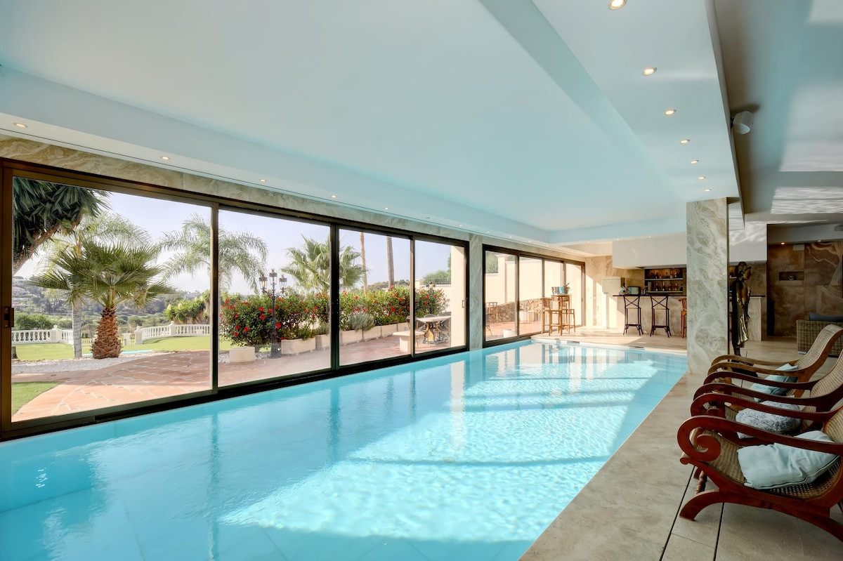 Indoor swimming pool with large windows overlooking greenery.