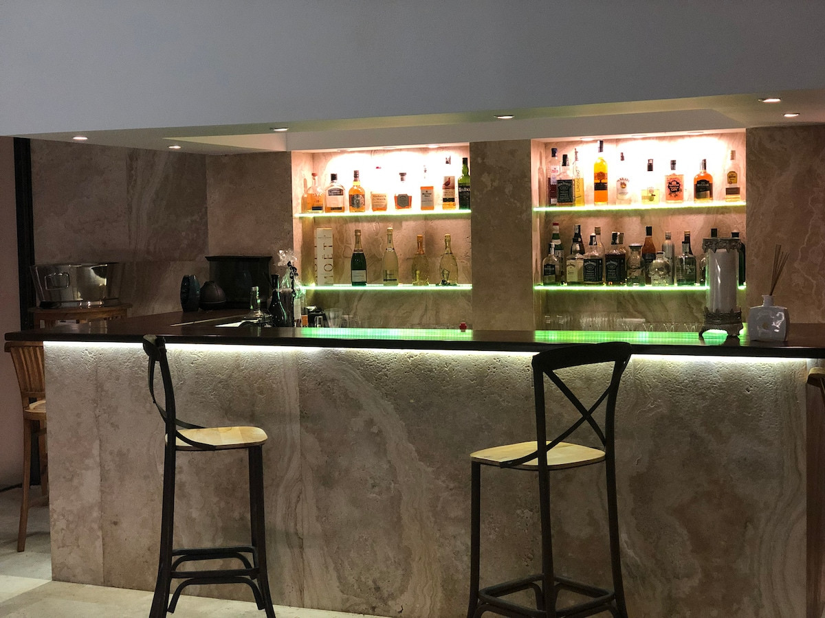 Stylish bar area with illuminated shelves displaying various bottles and bar stools.
