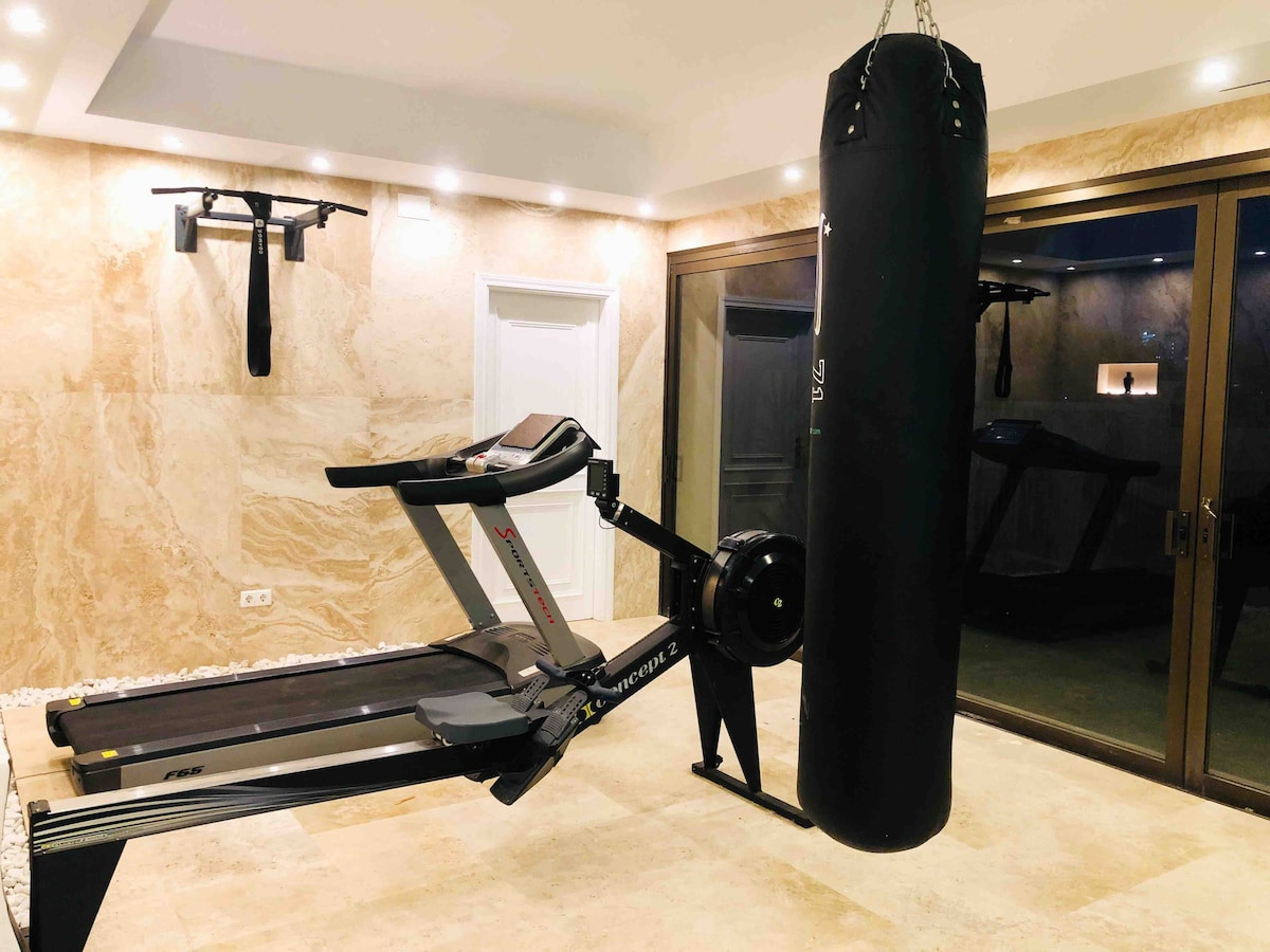 Modern gym area with exercise equipment, boxing bag, and warm lighting.