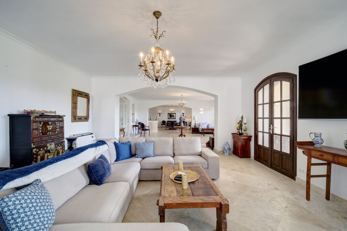 Living room with chandelier, sofa, and decorated cabinets in the background.