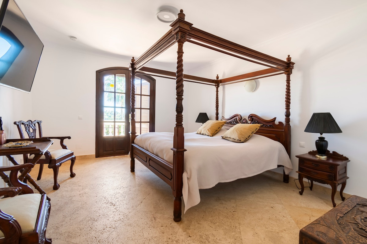 Elegant four-poster bed with decorative pillows and a view outside from the window.