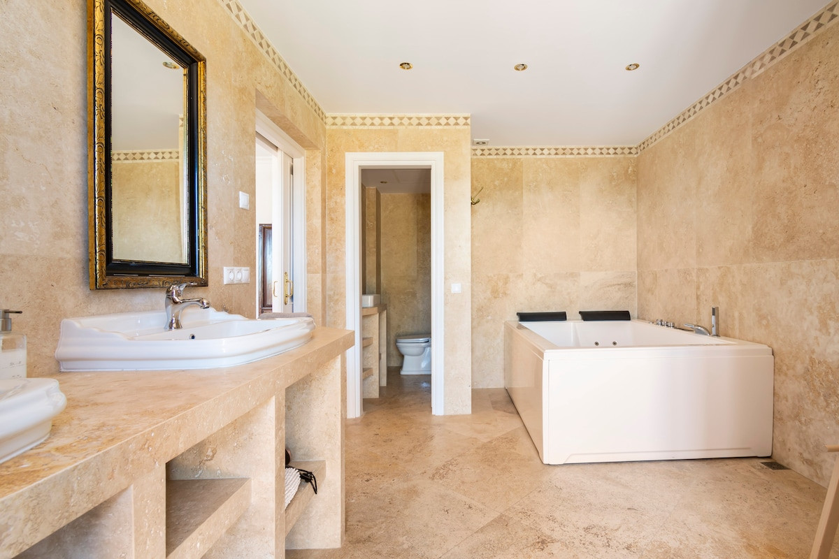 Spacious bathroom with a large tub and dual sinks, accented by beige marble walls.