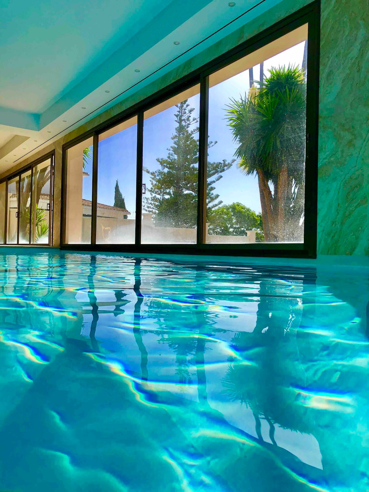 Indoor pool with reflections and palm trees visible through large windows.