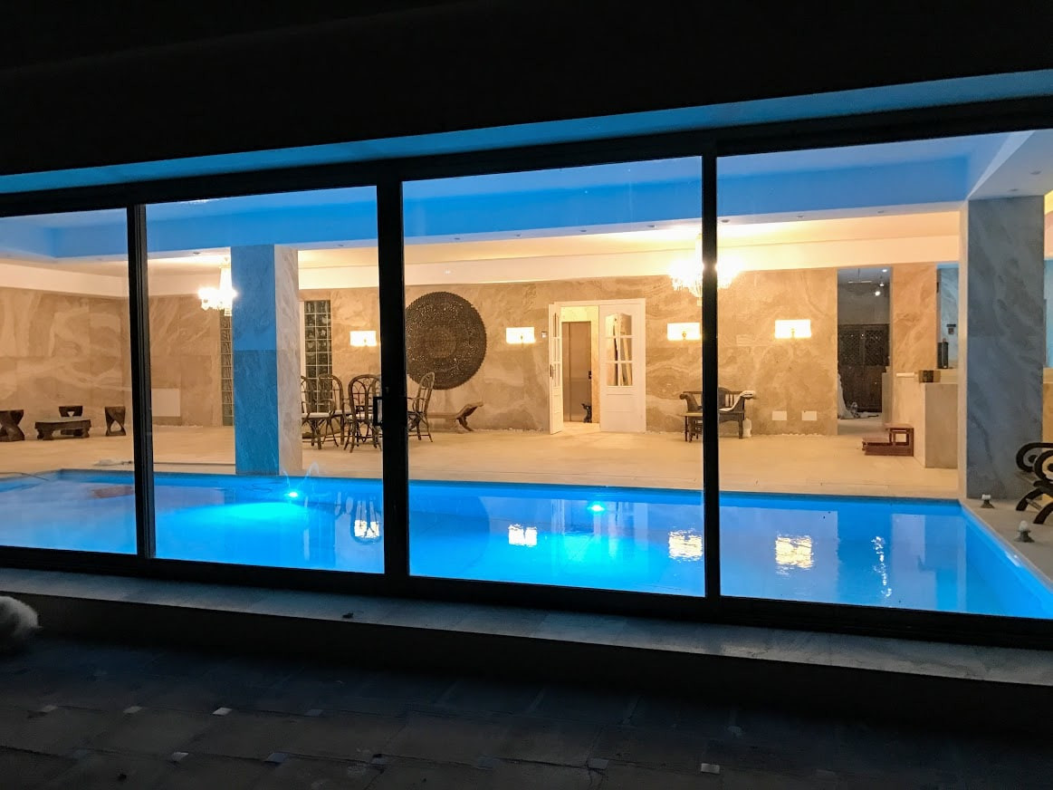Indoor swimming pool area visible through large glass doors, illuminated by overhead lighting.
