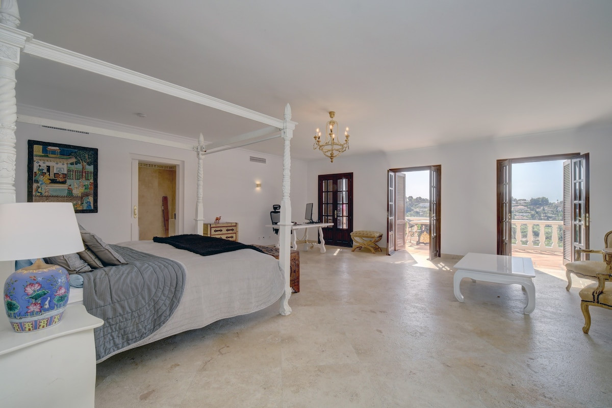 Bright bedroom with a chandelier, two balconies, and a four-poster bed.
