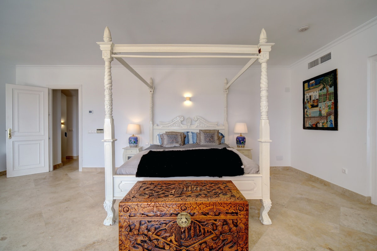 Canopy bed with decorative pillows and art, illuminated by lamps in a spacious bedroom.