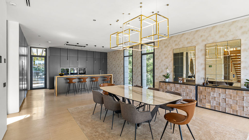 Dining area featuring a large table, stylish chairs, unique light fixtures, and gold accent mirrors on the wall.