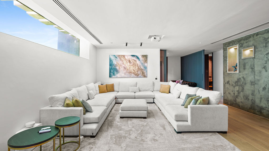 Bright living area with a large sectional sofa and a painting above, windows allowing natural light.