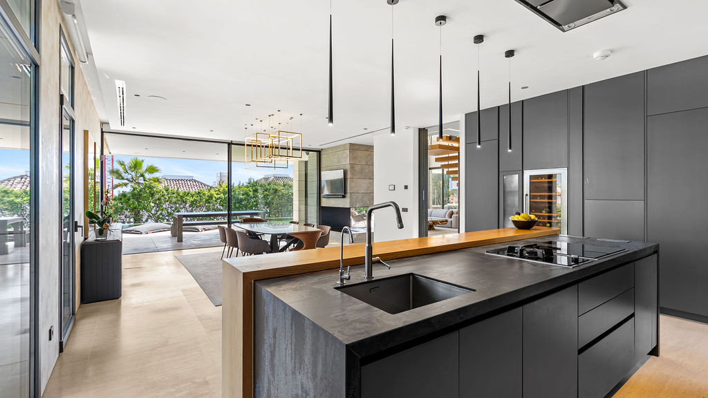 Modern kitchen with island, dark cabinetry, wine cooler, and views of the outdoor seating area.