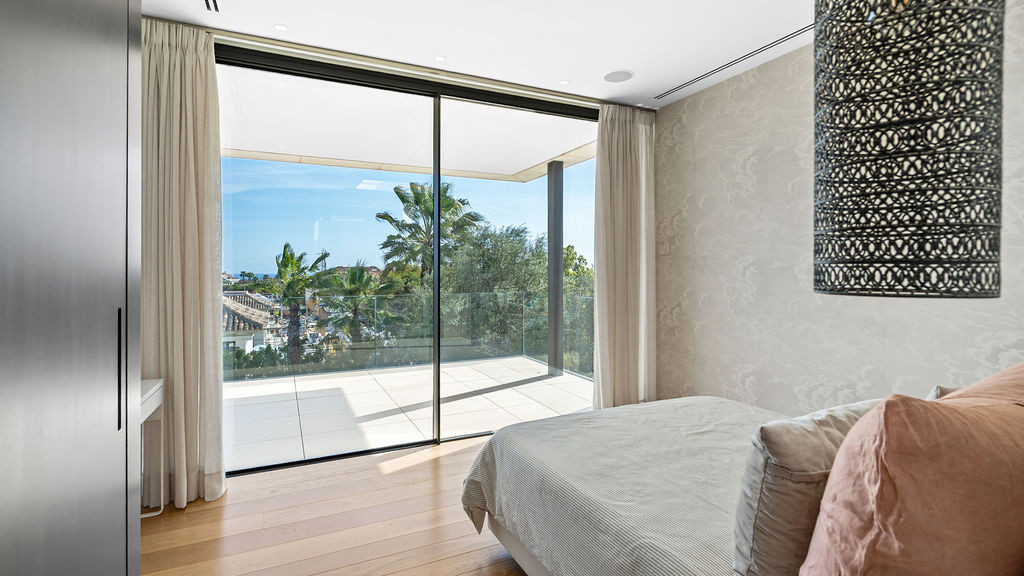 Stylish bedroom featuring large glass doors and palm view.