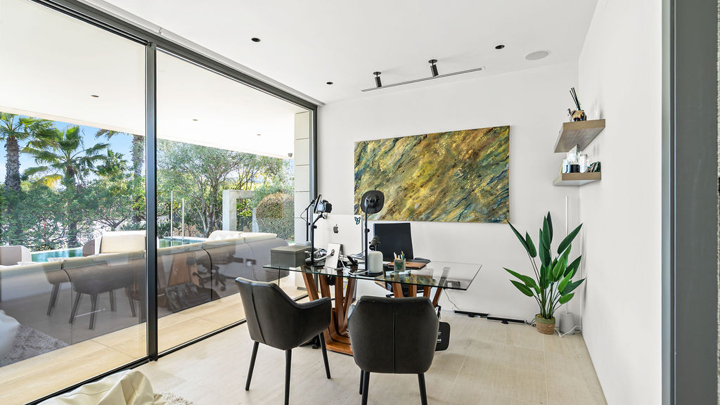 Home office with a glass wall, desk, and tropical plants.