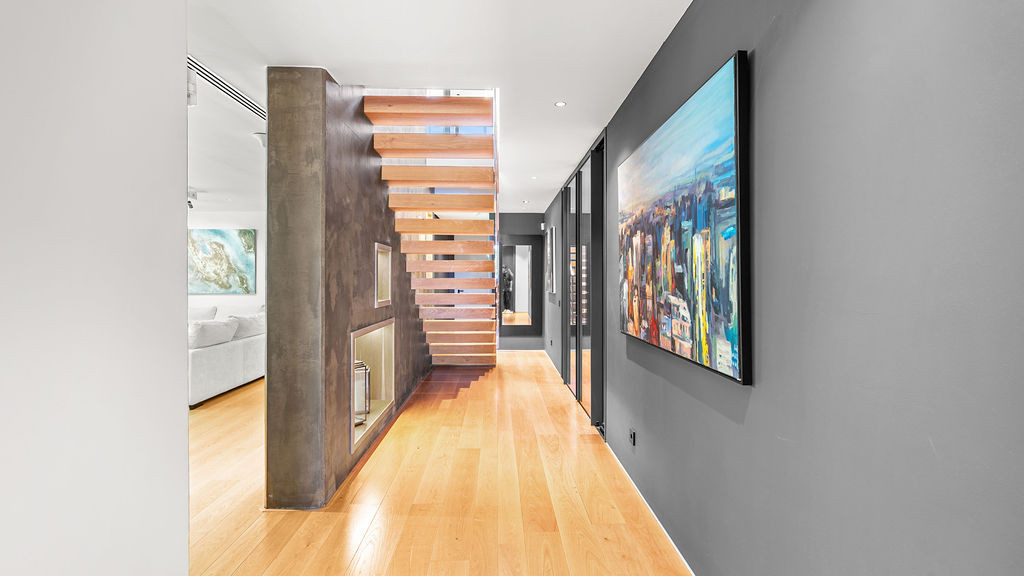 Spacious hallway with wooden floors and a modern staircase, featuring artwork on gray walls.