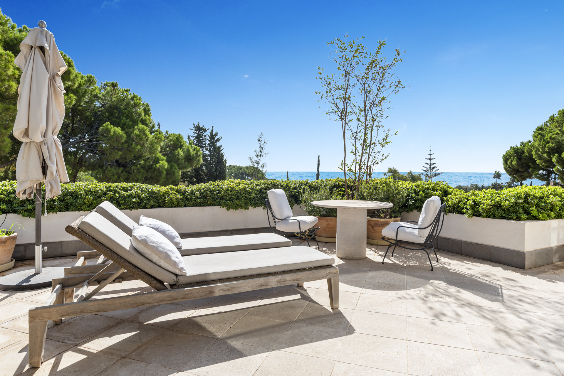 Relaxing terrace with sun loungers, a table, and views of the ocean and surrounding greenery.