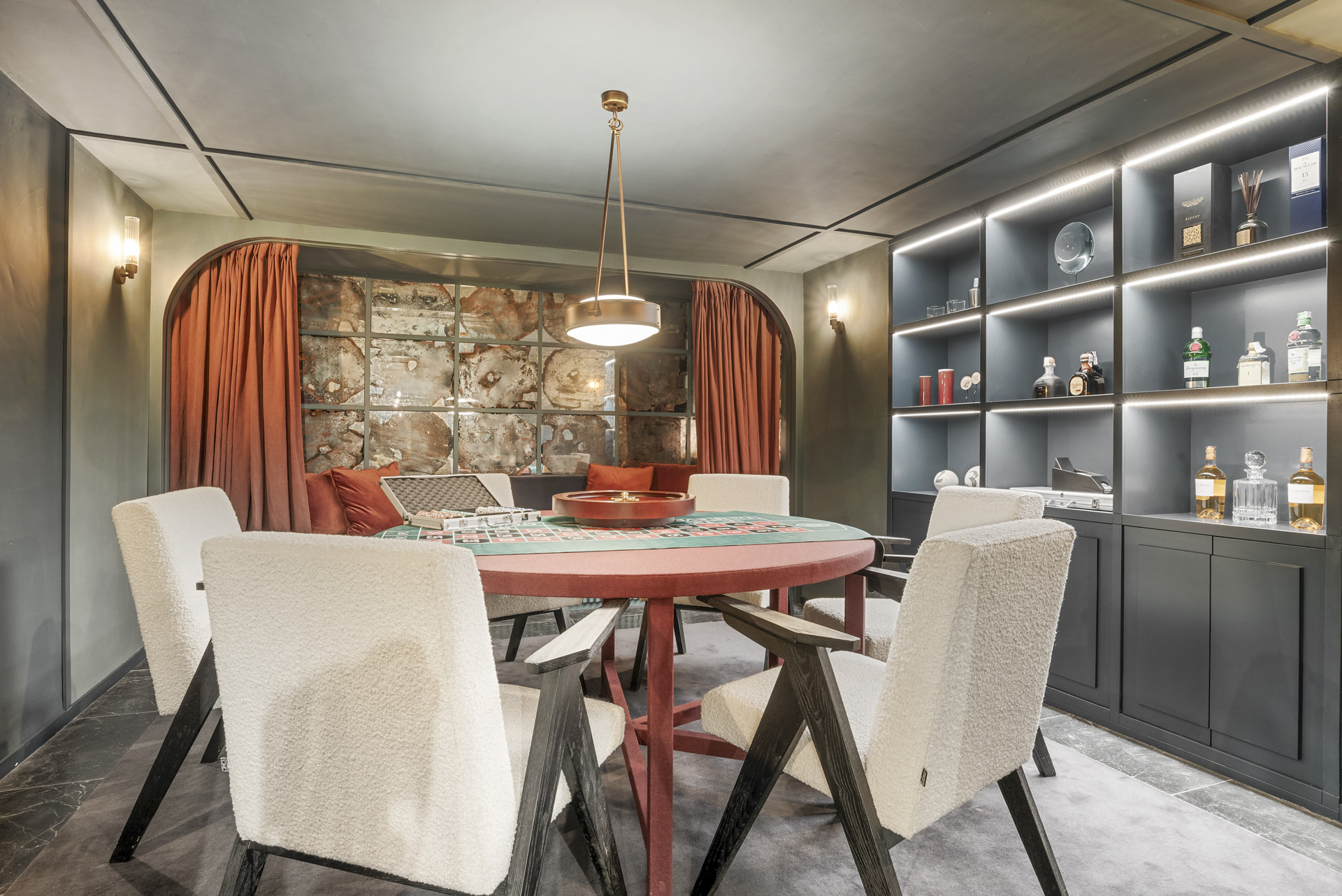 Elegant game room with a round table, plush chairs and curated drinks display.