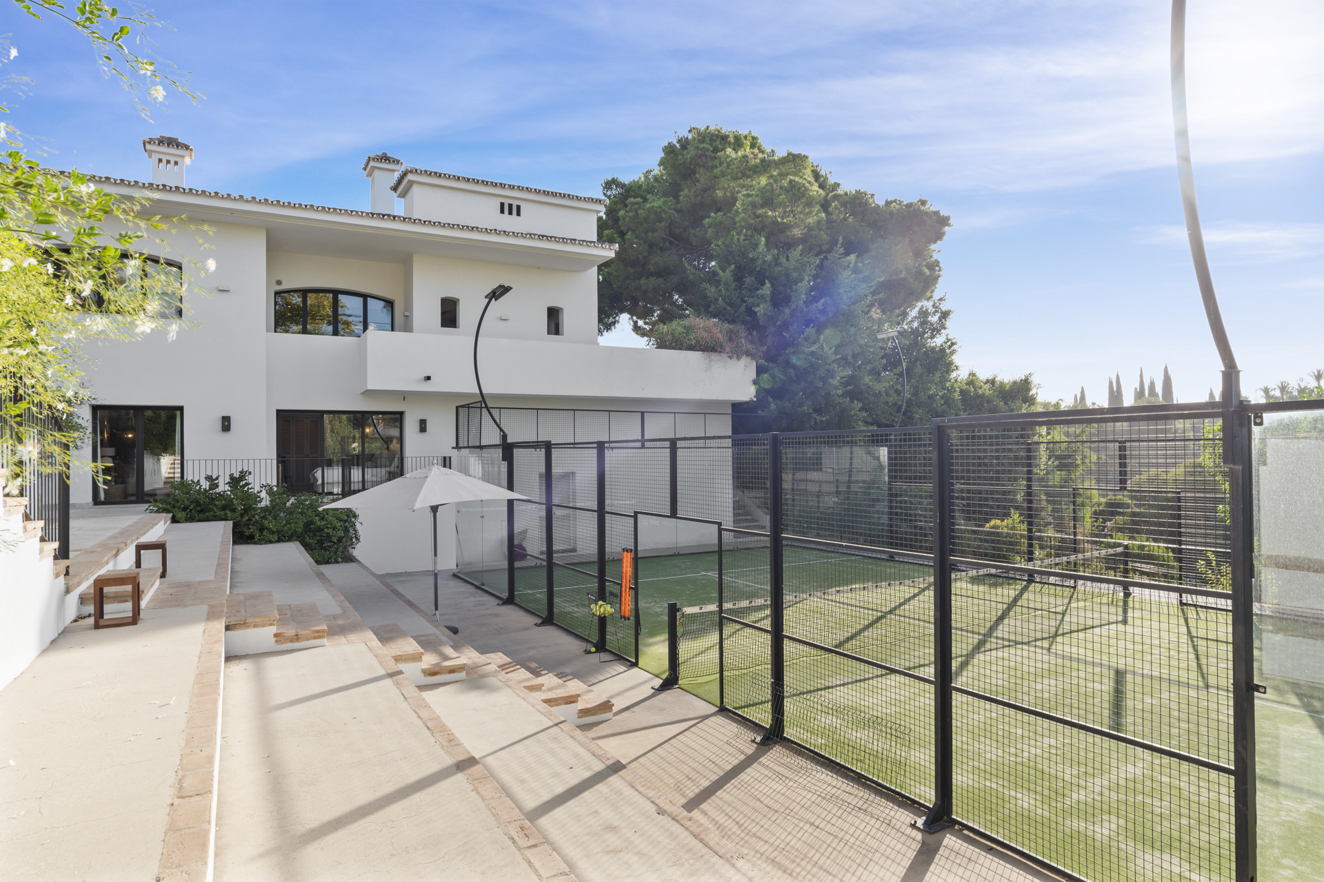 View of the back yard featuring a tennis court and a white umbrella near the house.