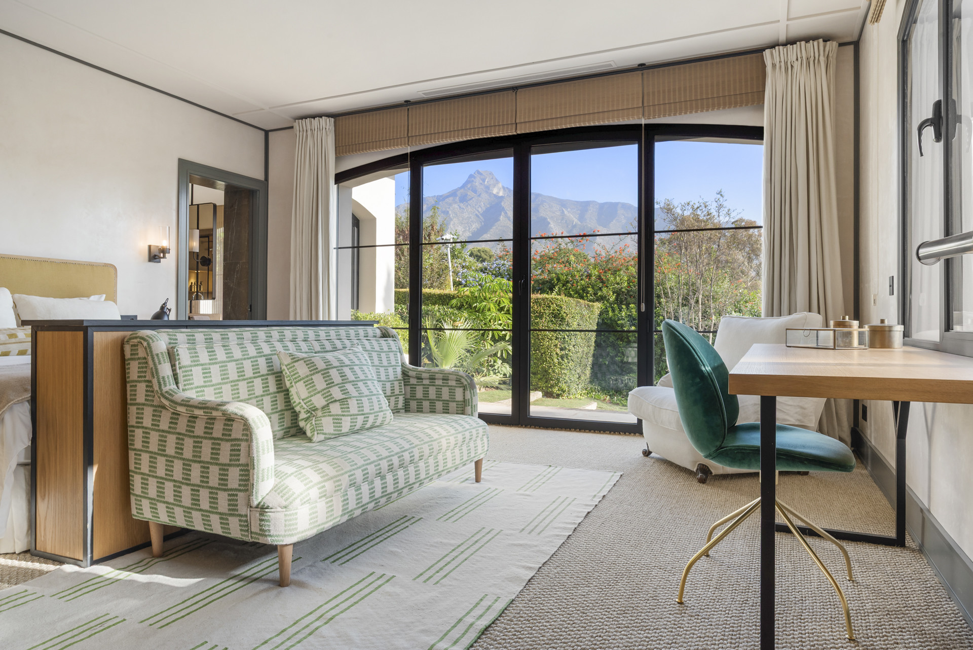 Alternate angle of the bedroom with a green sofa and desk furniture near large glass windows.