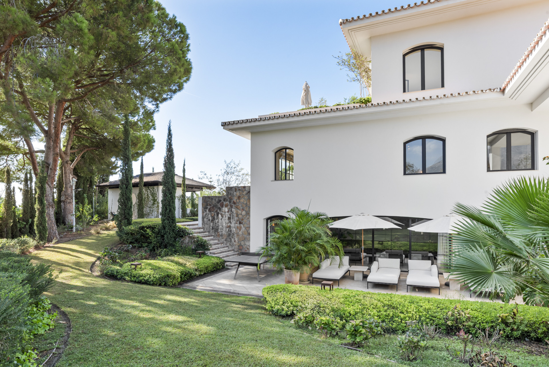 Exterior view of the house surrounded by landscaped gardens and lounge chairs.