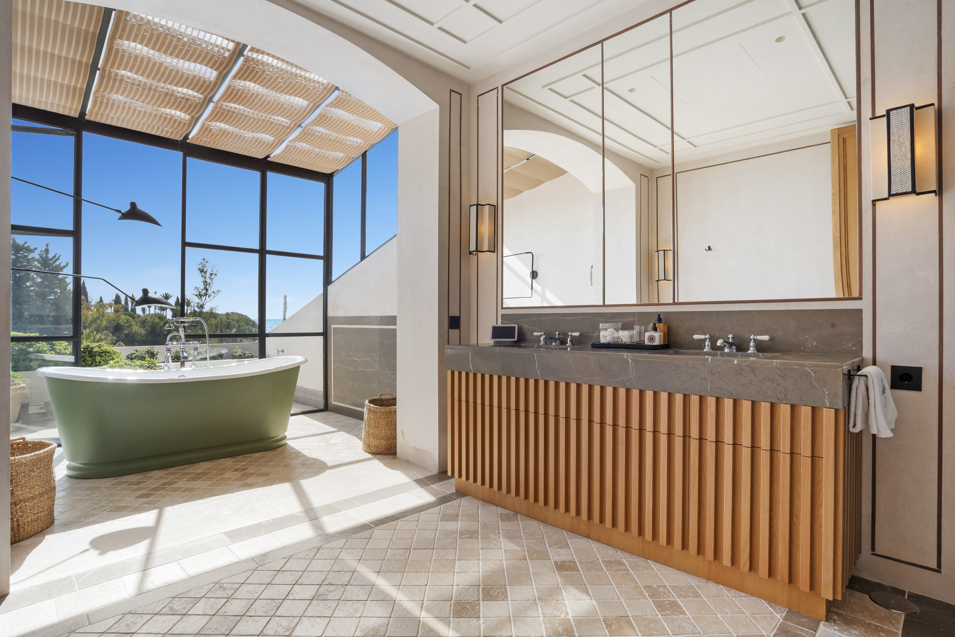 Spacious bathroom with a green bathtub, double sink, and large windows showcasing garden views.