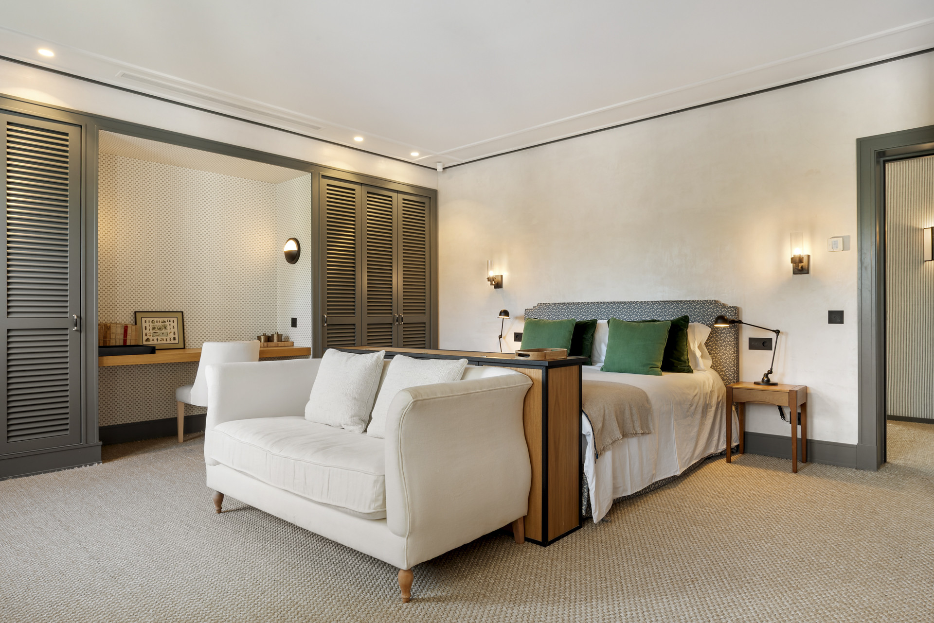 Spacious bedroom with a large bed, green pillows, and seating area; built-in cabinets in background.