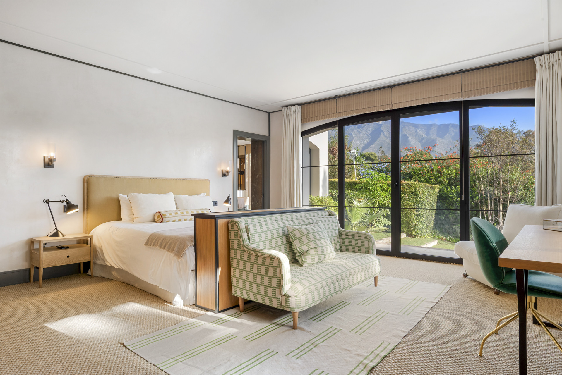 Spacious bedroom with a sofa, desk, and large windows showing mountain views.