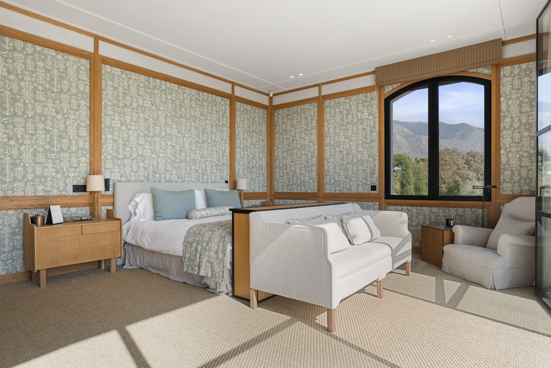 Spacious bedroom with patterned wallpaper, large bed and seating area.