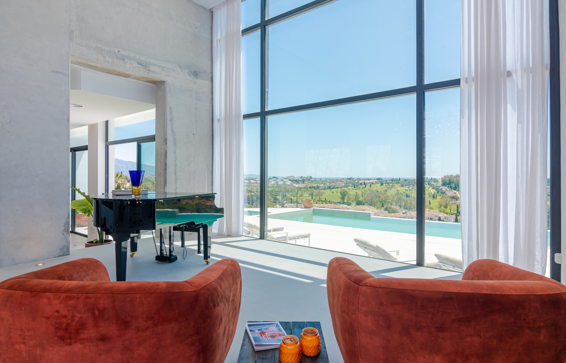 A living area with large windows showcasing a pool view and a grand piano in the foreground.